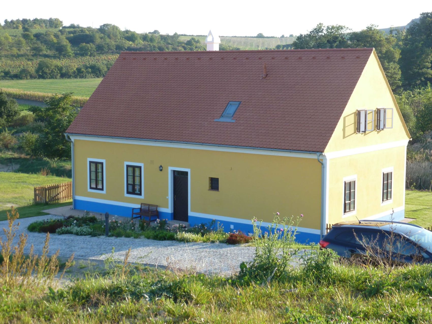 Žlutá chalupa s modrým soklem a zahradou s vinicí v pozadí